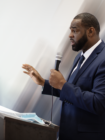 Getro Elize speaking at podium holding microphone.