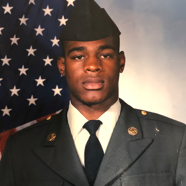 Portrait of Getro Elize in U.S. Army soldier uniform beside an American flag.