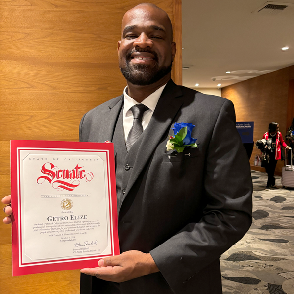 Getro Elize wearing suit holding a Senate certificate of recognition