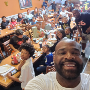 Getro Elize taking a selfie smiling in front of community members in restaurant in celebration