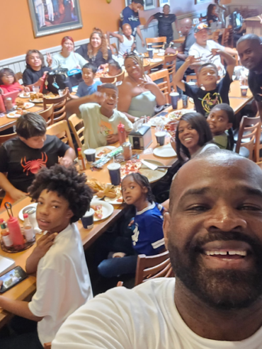 Getro Elize taking a selfie smiling in front of community members in restaurant in celebration