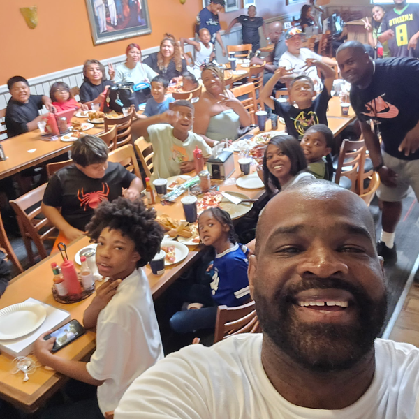 Getro Elize taking a selfie smiling in front of community members in restaurant in celebration