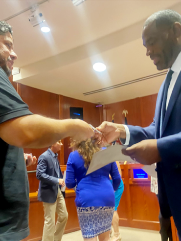 Getro Elize in a suit hands paperwork to another man in a meeting room.