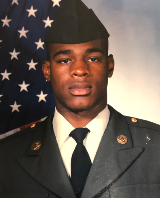 Portrait of Getro Elize in U.S. Army soldier uniform beside an American flag.