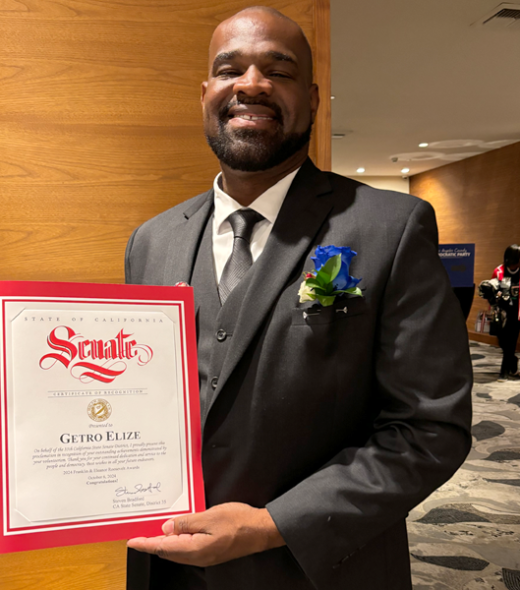 Getro Elize wearing suit holding a Senate certificate of recognition
